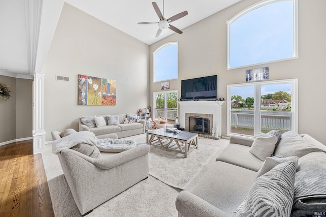 living room featuring decorative columns, high vaulted ceiling, ceiling fan, wood finished floors, and a brick fireplace