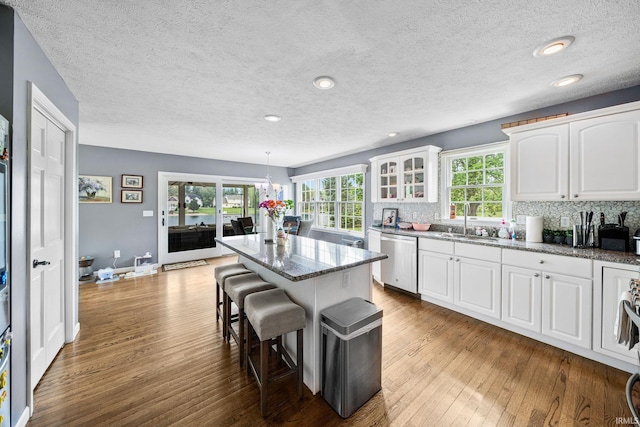 kitchen with stainless steel dishwasher, a sink, a breakfast bar, hardwood / wood-style flooring, and white cabinetry