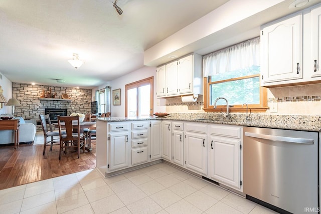kitchen featuring stainless steel dishwasher, a peninsula, a stone fireplace, and light stone counters