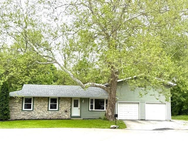 view of front facade featuring driveway, stone siding, and a front yard