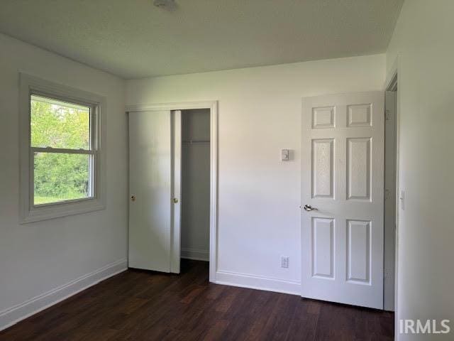 unfurnished bedroom featuring dark wood finished floors, a closet, and baseboards