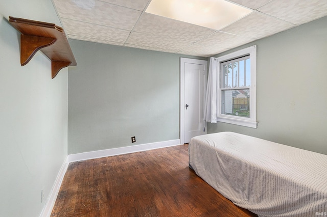 bedroom with wood finished floors, baseboards, a drop ceiling, and a closet