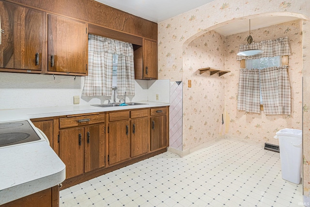 kitchen featuring a sink, wallpapered walls, light countertops, brown cabinetry, and electric range