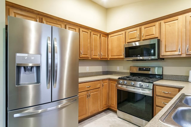 kitchen featuring appliances with stainless steel finishes, a sink, light countertops, and brown cabinetry