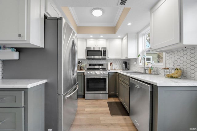 kitchen featuring appliances with stainless steel finishes, a sink, ornamental molding, light wood-style flooring, and gray cabinetry