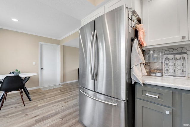kitchen with freestanding refrigerator, gray cabinets, light wood-type flooring, backsplash, and light stone counters