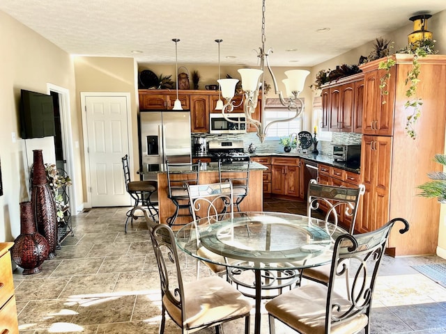 kitchen with stainless steel appliances, stone tile flooring, a kitchen island, backsplash, and dark countertops