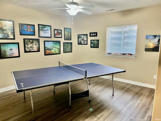 recreation room with wood finished floors, baseboards, ceiling fan, and a textured ceiling