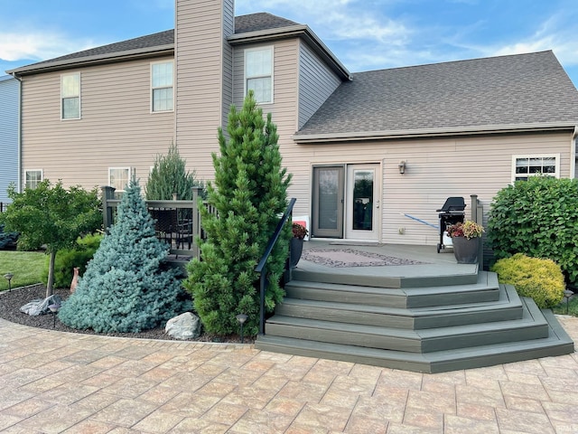 rear view of property featuring a chimney and roof with shingles