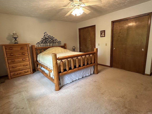 bedroom with a textured ceiling, light colored carpet, ceiling fan, and two closets