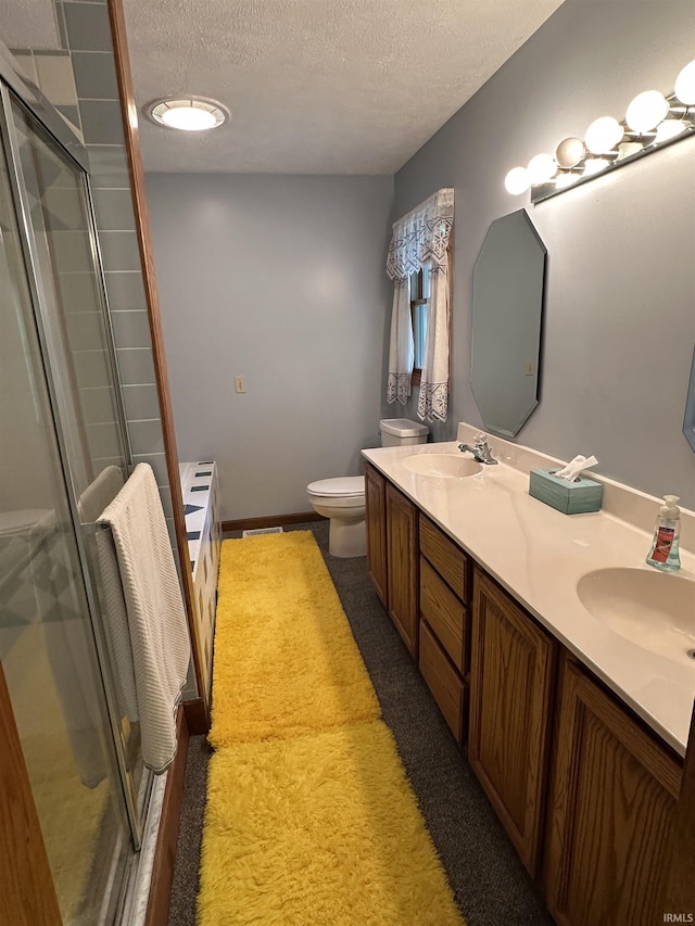 bathroom with toilet, a textured ceiling, a shower stall, double vanity, and baseboards