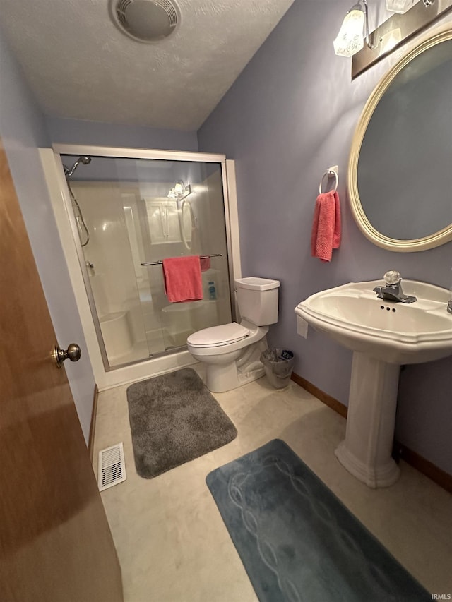 bathroom featuring toilet, a shower stall, baseboards, and a textured ceiling