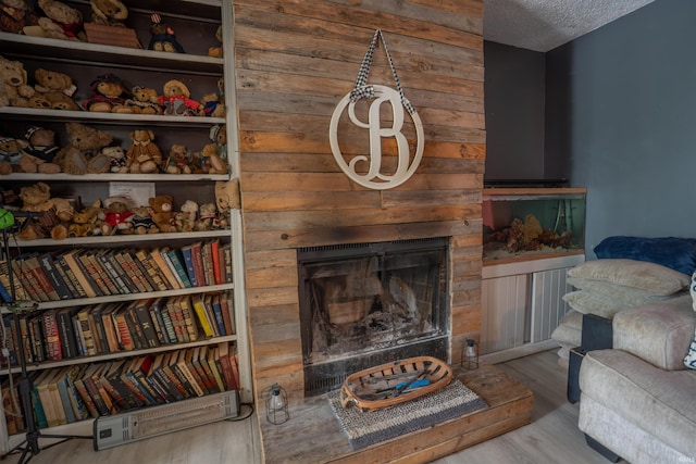 living area with wood finished floors, a fireplace with raised hearth, and a textured ceiling