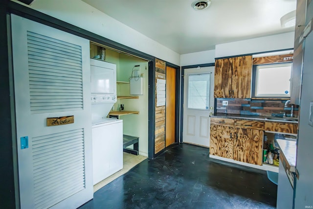 kitchen with stacked washing machine and dryer, a sink, and concrete flooring