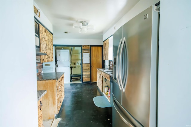 kitchen with stainless steel fridge with ice dispenser, stacked washer / dryer, and finished concrete floors