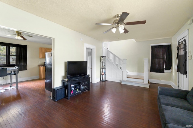 living area with a ceiling fan, dark wood-style flooring, baseboards, and stairway