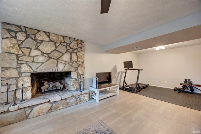 workout area with wood finished floors, a textured ceiling, a stone fireplace, and baseboards