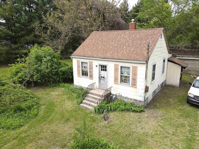 view of front of property with a shingled roof, a chimney, and a front lawn