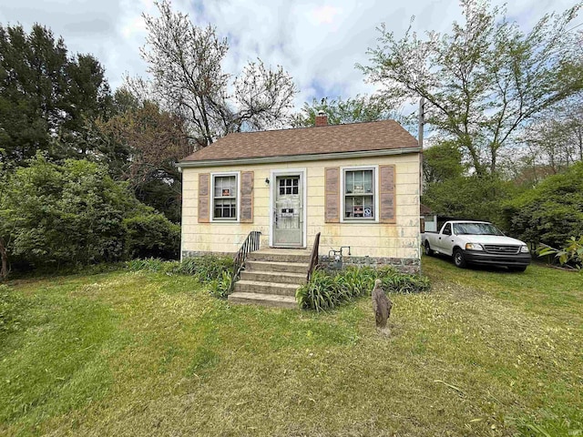 bungalow-style house featuring a chimney, a front yard, and roof with shingles