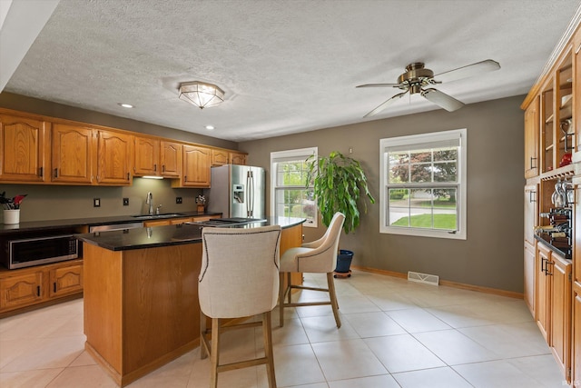 kitchen featuring stainless steel fridge with ice dispenser, a sink, a center island, a breakfast bar area, and dark countertops