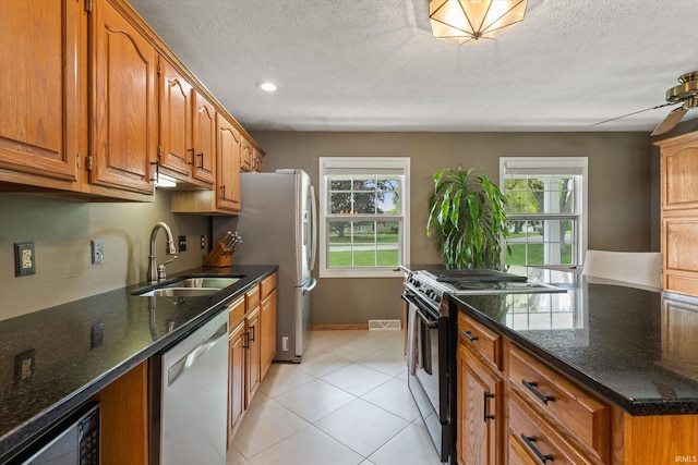 kitchen with appliances with stainless steel finishes, a sink, healthy amount of natural light, brown cabinets, and a textured ceiling