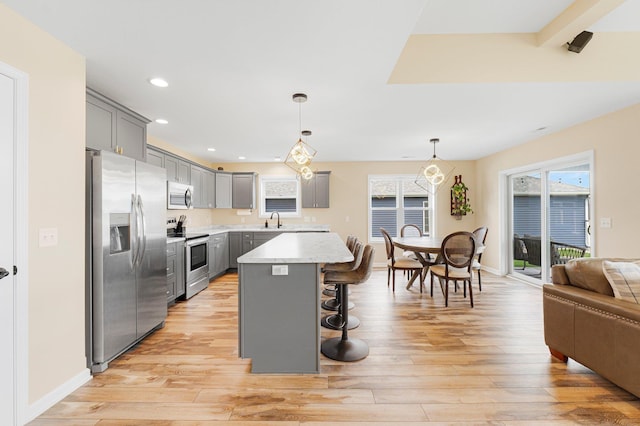 kitchen with appliances with stainless steel finishes, gray cabinets, a sink, a kitchen breakfast bar, and recessed lighting