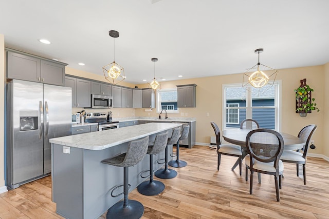 kitchen featuring appliances with stainless steel finishes, light wood finished floors, baseboards, a breakfast bar area, and gray cabinets