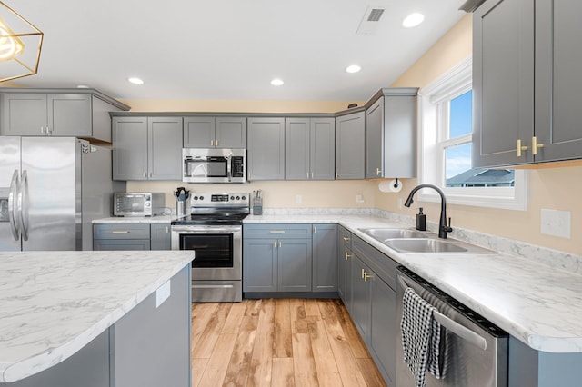 kitchen featuring appliances with stainless steel finishes, a sink, gray cabinets, light wood finished floors, and recessed lighting