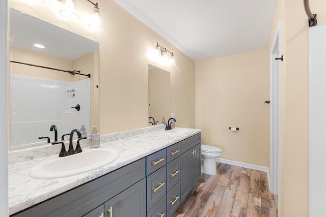 bathroom featuring wood finished floors, toilet, double vanity, and baseboards