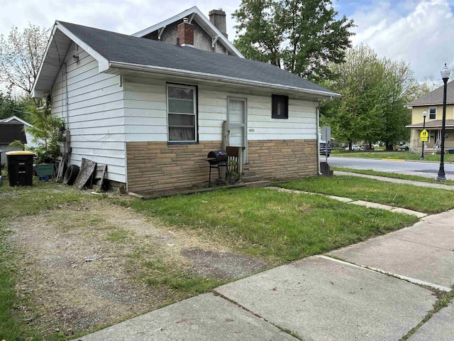 view of front of house with a chimney, stone siding, and a front lawn