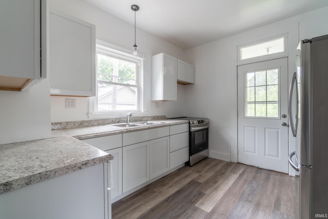 kitchen featuring appliances with stainless steel finishes, a sink, light wood finished floors, light countertops, and pendant lighting