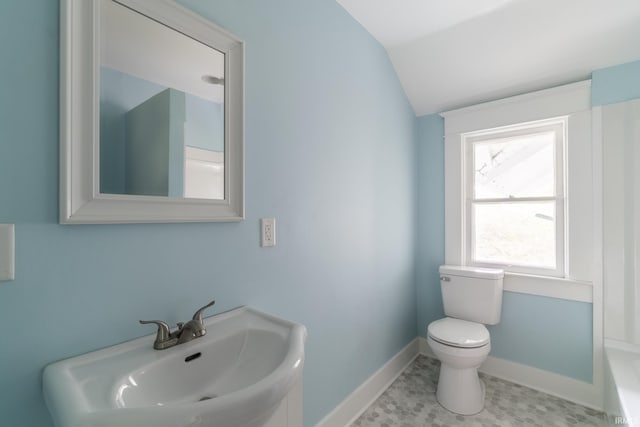 bathroom with a sink, toilet, lofted ceiling, baseboards, and a tub to relax in