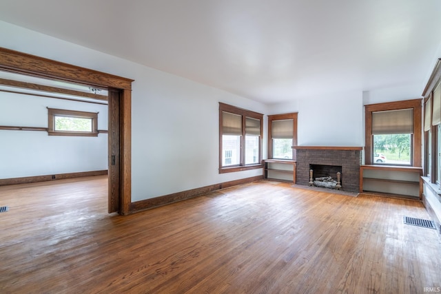 unfurnished living room featuring plenty of natural light, wood finished floors, a brick fireplace, and baseboards