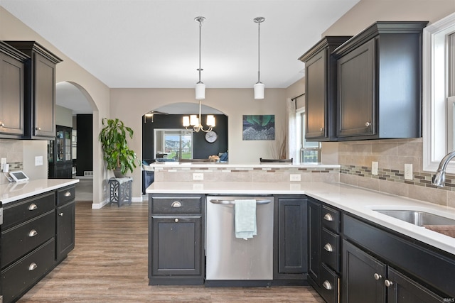 kitchen featuring dishwasher, a peninsula, arched walkways, backsplash, and a sink