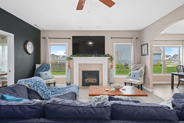 living area featuring arched walkways, ceiling fan, a tile fireplace, and baseboards