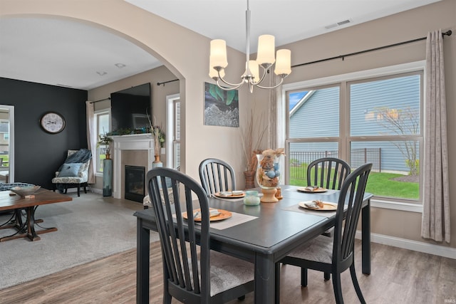 dining room featuring a chandelier, light wood-style floors, arched walkways, a glass covered fireplace, and baseboards