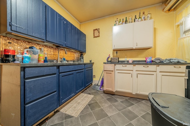 kitchen featuring blue cabinetry, dark tile patterned flooring, dark countertops, and a sink
