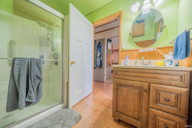 bathroom featuring a shower stall, wood finished floors, wainscoting, vanity, and wood walls