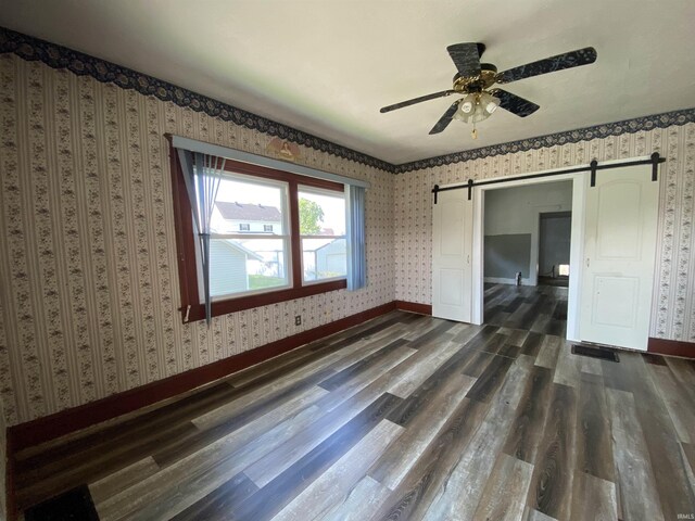 1107 S St, Bedford, IN 47421 - spare room featuring a barn door, wallpapered walls, dark wood finished floors, ceiling fan, and baseboards