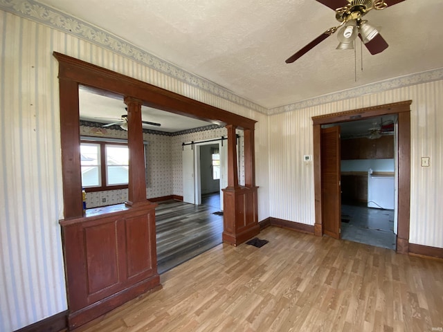 1107 S St, Bedford, IN 47421 - unfurnished room featuring light wood-style flooring, a ceiling fan, wallpapered walls, a barn door, and baseboards