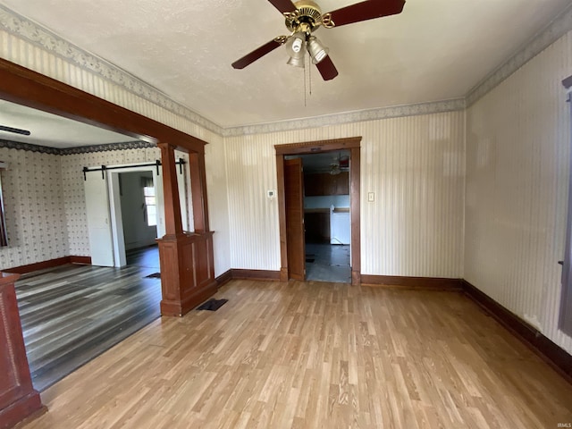 1107 S St, Bedford, IN 47421 - unfurnished room with a barn door, wood finished floors, baseboards, ceiling fan, and wallpapered walls