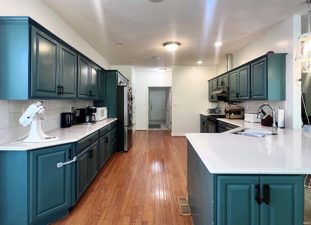 kitchen featuring a sink, white microwave, freestanding refrigerator, a peninsula, and light wood-style floors