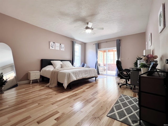 bedroom featuring access to outside, light wood-style flooring, a textured ceiling, a desk, and ceiling fan