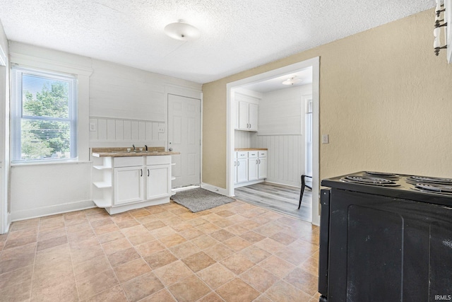 kitchen with black range with electric stovetop, a textured ceiling, white cabinets, a sink, and a textured wall