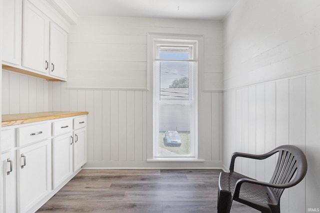 kitchen with light wood-type flooring, white cabinetry, wood walls, and wood counters