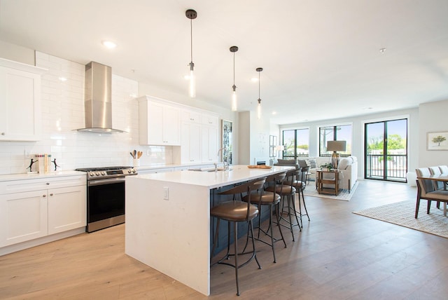 1740301W S Bend Ave, South Bend, IN 46637 - kitchen with gas range, wall chimney exhaust hood, backsplash, an island with sink, and light wood-style floors