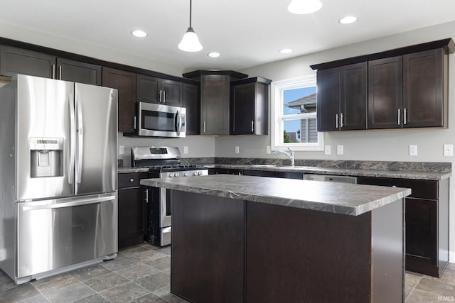 kitchen with stainless steel appliances, dark countertops, a sink, dark brown cabinetry, and a center island