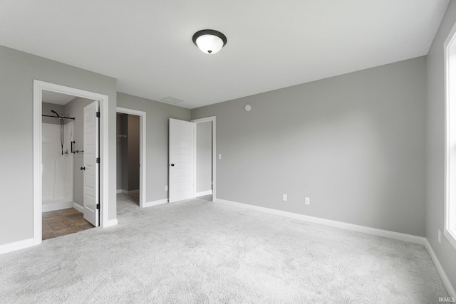 unfurnished bedroom featuring carpet floors, baseboards, ensuite bath, a spacious closet, and a closet