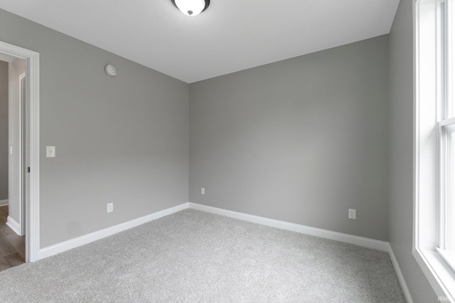 carpeted spare room featuring baseboards and a smoke detector