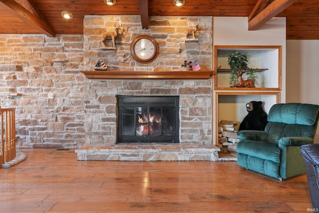 living area with wooden ceiling, beamed ceiling, wood-type flooring, and a stone fireplace